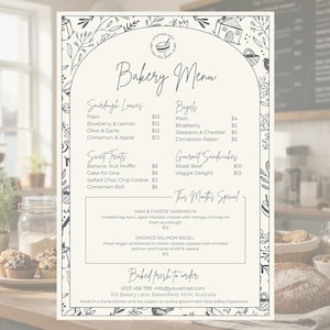 Könnte beinhalten: Ein Bäckereimenü auf cremefarbenem Hintergrund mit handschriftlicher Schrift. Die Speisekarte listet Sauerteigbrote, Bagels, süße Leckereien, Gourmet-Sandwiches und ein Special auf. Florale und Hausillustrationen schmücken den Rand.