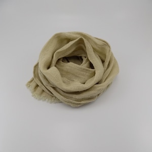 May include: A beige scarf made of a loosely woven fabric. The scarf is draped in a circular pattern, with the ends slightly frayed. The neutral color and texture suggest a lightweight, breathable accessory.