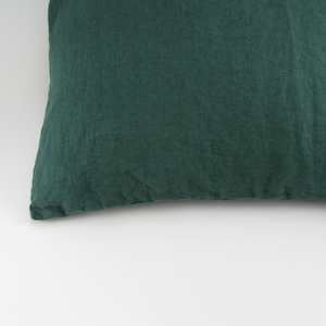 May include: A dark green pillow with a textured linen fabric. The pillow is rectangular and appears to be filled with a soft material. The fabric has a slightly wrinkled appearance.