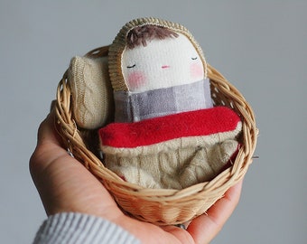 holiday mini baby doll, swaddled baby, in a vintage basket with wool blanket and cushion, grey and white checkered fabric, gold bonnet