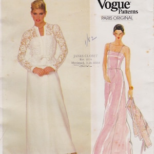 May include: A Vogue Patterns Paris Original sewing pattern envelope featuring a white long-sleeved dress with lace detailing and a pink floor-length gown with thin straps. The text includes Vogue Patterns, Paris Original, and Janes Closet Rte. 101A Merrimack, N.H. 03054.