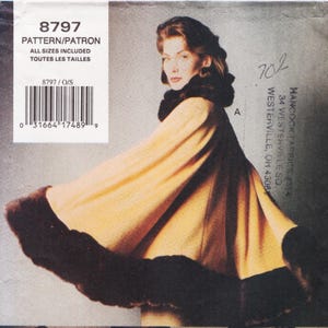 May include: A sewing pattern envelope labelled 8797 featuring a tan cape with a dark brown fur collar and hem trim. The envelope includes a barcode, the text PATTERN/PATRON, and ALL SIZES INCLUDED. The design shows a flared silhouette with fur accents.