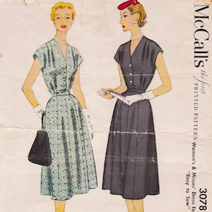 May include: Vintage McCall's sewing pattern featuring illustrations of two dresses. One dress is light blue with a patterned design, the other is dark gray. The pattern includes the text "Easy to Sew".