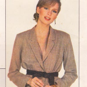 May include: A light brown blazer with a black belt. The blazer has a classic design with a notched lapel and a tailored fit. The black belt cinches the waist, creating a defined silhouette. The blazer is made of a textured fabric.