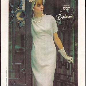 May include: A vintage fashion illustration featuring a light gray dress with short sleeves and a fitted silhouette. The image includes the text "pattern 1327 by Balmain". The model is wearing a pearl necklace and gloves.