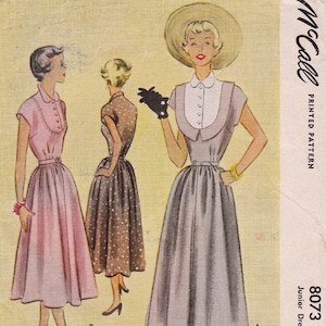 May include: Vintage McCall printed pattern featuring illustrations of three dresses. The dresses are in shades of pink, brown, and gray, with details like collars, belts, and full skirts. The pattern is labeled "8073 Junior Dress."