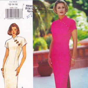 May include: A sewing pattern for a mandarin collar dress in sizes 12-14-16. The pattern includes a drawing of a white dress with floral accents and a bright pink dress with gold-colored buttons. The pattern is from Hancock Fabrics.