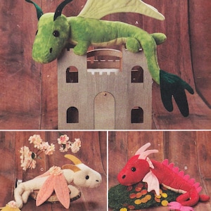 May include: Three plush dragon toys in different colours. A green dragon with black horns and wings sits on a wooden castle. A red dragon with pink spines and wings lies on a green surface. A white dragon with pink ears and yellow horns is also shown.