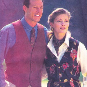 May include: A man and woman are wearing vests. The man is wearing a burgundy vest over a blue button-down shirt and patterned tie. The woman is wearing a navy vest with a colorful pattern over a white collared shirt.