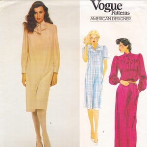 May include: Vogue Patterns American Designer sewing pattern featuring three different dress designs. The dresses include a long-sleeved beige dress with a bow, a blue plaid dress, and a long pink dress with a bow.