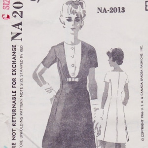 May include: Vintage sewing pattern featuring a woman in a dark dress with a white collar and bow detail. The pattern includes a second dress design. Text includes "NA-2013" and copyright information.