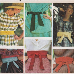 May include: A collection of six fabric waist sashes shown in various colors including yellow, dark green, cream, light blue, red, and orange. Each sash is tied in a simple front knot and worn over different garments like dresses and skirts.