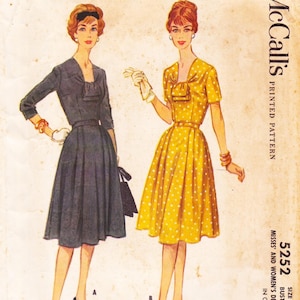 May include: A vintage McCall's 5252 printed sewing pattern envelope featuring illustrations of two dresses. One is a solid dark gray dress with three-quarter sleeves, and the other is a yellow dress with white polka dots and short sleeves.