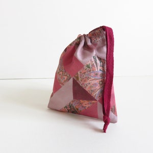 May include: A pink and burgundy drawstring bag with a paisley pattern. The bag has a burgundy drawstring.
