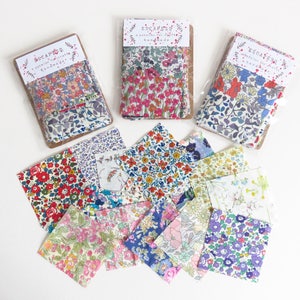 May include: Fabric bundles with floral patterns in various colors, including red, pink, blue, and purple. The bundles are packaged with a cardboard header that reads "ESCAPE a selection for creative handmade". Several fabric squares are scattered around the bundles.