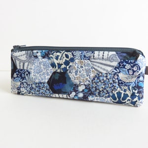 May include: A blue and white patchwork fabric pencil case with a zipper closure and a grey pull tab.