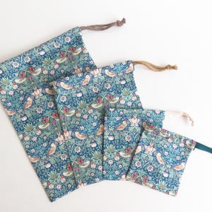 Peut inclure: Un ensemble de quatre sacs à cordon de serrage de tailles variées. Les sacs présentent un motif floral bleu sarcelle avec des oiseaux, des fleurs et des feuilles. Chaque sac a un cordon de serrage de couleur différente.