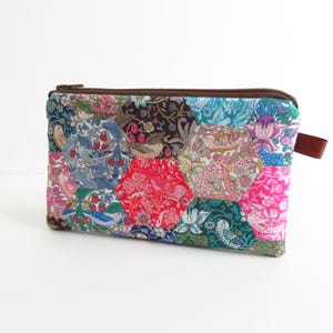 以下が含まれることがあります： 茶色のジッパーとプルタブが付いた、長方形のパッチワーク生地のポーチ。ポーチは、青、ピンク、赤、緑など、さまざまな色の六角形の生地片でできており、花柄や鳥柄が施されています。背景は白です。