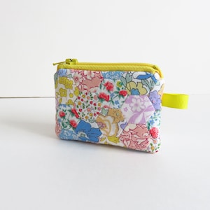 Peut inclure: Une petite pochette zippée jaune avec un imprimé floral. La pochette est en tissu et possède une fermeture éclair jaune et une tirette jaune.