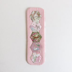 以下が含まれることがあります： ピンクと白のストライプの生地のしおりで、さまざまな花の模様の六角形の生地のパッチが5つ付いています。