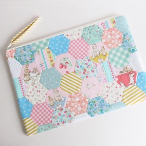 Könnte beinhalten: Eine gesteppte Tasche mit einem farbenfrohen Patchwork-Design. Die Tasche hat eine Vielzahl von sechseckigen Stoffstücken in Pastellfarben, darunter Rosa, Blau und Gelb. Das Design enthält Illustrationen von Kaninchen und Erdbeeren.