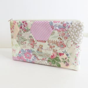 May include: A rectangular zipped pouch featuring a patchwork design of various fabric patterns, including floral prints, pink and white stripes, and illustrations of figures in a garden setting, all arranged in a hexagonal quilt-like layout.