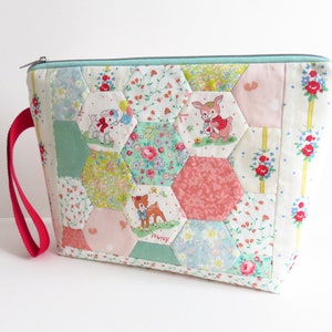 May include: A patchwork fabric zippered pouch with a red handle. The pouch is made of various floral prints and features a hexagonal pattern with appliqued animal figures. The animals include a deer, a bunny, and a lamb.
