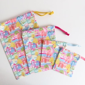 Puede incluir: Conjunto de cuatro bolsas de cordón de diferentes tamaños. Las bolsas están hechas de una tela ligera con un estampado de ciudad colorido en rosa, azul y amarillo. Las bolsas tienen un cierre de cordón y son perfectas para guardar objetos pequeños.