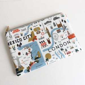 Puede incluir: Una bolsa blanca con cremallera con un diseño de mapa que muestra ilustraciones de lugares emblemáticos de Ciudad de México y Londres. El diseño incluye el London Eye, el Big Ben y un autobús de dos pisos rojo. Los textos "Mexico City" y "London" son visibles.