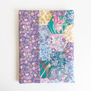 May include: A purple, blue, green and pink fabric pouch with a hexagonal patchwork design. The pouch is made of various floral patterned fabrics.