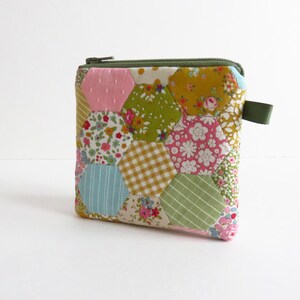 以下が含まれることがあります： カラフルなキルトの小銭入れ。ファスナー開閉式。ピンク、緑、黄色、青など、様々な花柄や幾何学模様のパッチワークデザイン。側面に小さな緑色の布ループが付いています。
