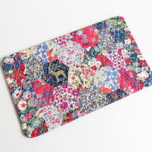 May include: A patchwork fabric pouch with a floral pattern in shades of pink, red, blue, and white. The pouch is quilted and has a hexagonal design.