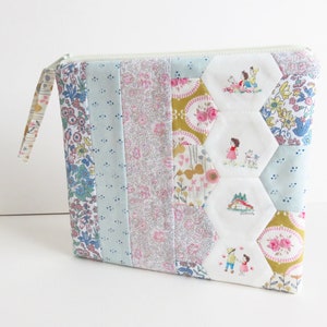 May include: A white zippered pouch with a patchwork design featuring floral fabric in shades of blue, pink, and yellow. The pouch has a hexagonal pattern with embroidered images of children and animals.