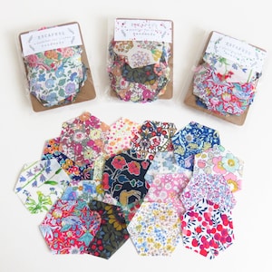 May include: A collection of floral fabric pieces in various colors and patterns. Some are packaged with tags that read "ESCAPESQ a passion for styles handmade". The fabric pieces are arranged on a white surface, showcasing a variety of floral designs.