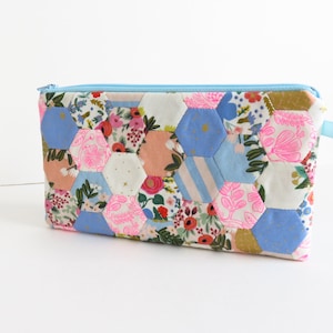 Może przedstawiać: Torebka z zamkiem błyskawicznym z tkaniny patchworkowej w kolorze niebieskim i różowym z sześciokątnym wzorem. Torebka jest wykonana z tkaniny bawełnianej i ma zamek błyskawiczny.