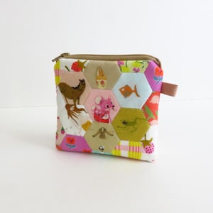 Op de afbeelding: Een kleine, vierkante, gewatteerde etui met ritssluiting. De etui is gemaakt van kleurrijke, bedrukte stof met diverse afbeeldingen, waaronder een paard, vis en muis. Het heeft een bruine rits en een kleine, roze stoffen lus aan de zijkant.