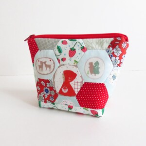 Peut inclure: Une pochette matelassée avec une fermeture éclair rouge et un motif patchwork. Le patchwork présente des motifs variés, notamment des fraises, des cerfs, une figure à capuche rouge et des imprimés floraux. La pochette est principalement rouge, blanche et bleu clair.