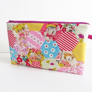 Peut inclure: Une pochette zippée rose et jaune avec un motif hexagonal. La pochette est faite de tissu avec différents imprimés, dont des animaux, des fleurs et des pois. La fermeture éclair est rose.