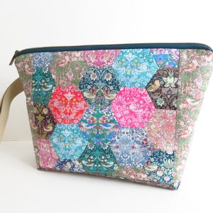 May include: A colorful, quilted pouch with a hexagonal pattern. The bag features a variety of floral and bird-themed fabrics in shades of pink, blue, green, and red. It has a teal zipper and a beige handle.