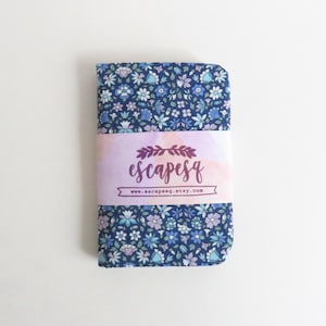 May include: A folded fabric item with a blue floral pattern, wrapped with a light purple band featuring the text "escapesq" and a website address. The fabric has a dark blue background with light blue and purple flowers.