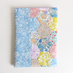 Puede incluir: Una cubierta de libro de tela azul con un diseño de patchwork de hexágonos en varios patrones florales, incluyendo rosa, amarillo y azul.