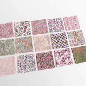 May include: An assortment of fifteen small, square fabric swatches. The swatches feature various floral and patterned designs in shades of pink, green, and white. The fabrics are arranged on a white surface.