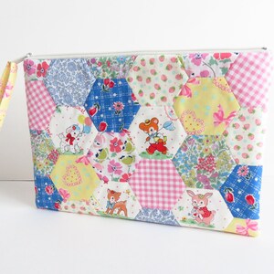 May include: A patchwork fabric zippered pouch with a yellow fabric handle. The pouch is made of various fabrics with different patterns, including pink and white gingham, blue and white floral, and yellow with pink hearts. The pouch features a variety of animal illustrations, including a bear, a deer, a rabbit, and a lamb.