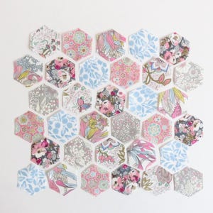 May include: A collection of 25 hexagon-shaped fabric patches in various floral patterns, including pink, blue, and white. The patches are arranged in a honeycomb pattern.