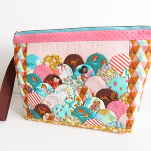 May include: A handmade, quilted pouch with a colorful, scalloped design. The pouch features a variety of patterned fabrics in pink, teal, yellow, and brown. A brown strap and a gold zipper complete the design. The pouch is approximately 10 inches wide.