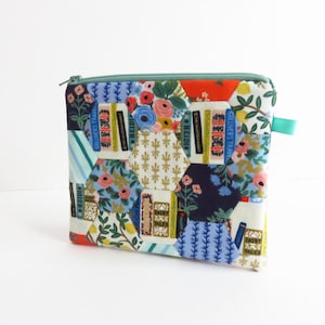 Può includere: Una pochette con cerniera in tessuto patchwork con un tiretto di chiusura in turchese. Il tessuto presenta un motivo esagonale con una varietà di colori e disegni, tra cui motivi floreali, dorsi di libri e forme geometriche.