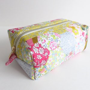 Può includere: Una trousse da toilette rettangolare in tessuto patchwork con una cerniera dorata. La trousse è realizzata con diversi tessuti a motivi floreali in tonalità rosa, giallo, blu e verde.