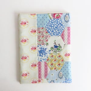 Puede incluir: Una funda de tela rectangular con un diseño de patchwork. El lado izquierdo presenta una tela verde claro con estampados florales rosas. El lado derecho tiene un patchwork de telas hexagonales y rectangulares.