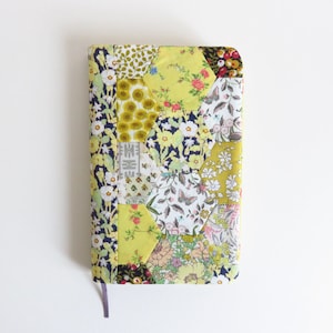 May include: A yellow and green fabric notebook cover with a patchwork design of floral and geometric patterns.