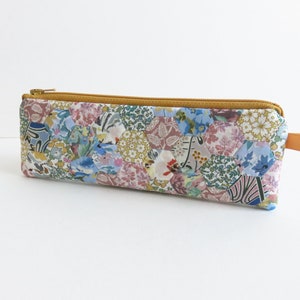 May include: A patchwork pencil case with a zipper closure and a yellow strap. The case is made of fabric with a variety of floral and geometric patterns in shades of blue, pink, green, and yellow.
